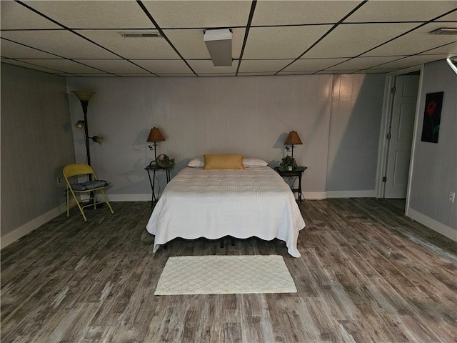 bedroom featuring visible vents, a drop ceiling, baseboards, and wood finished floors