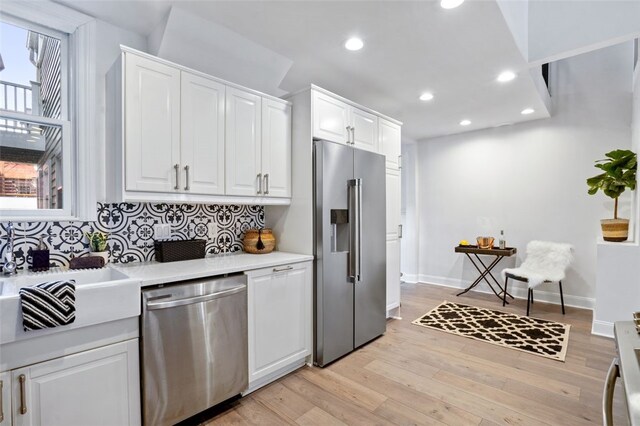 kitchen with light countertops, backsplash, light wood-style flooring, appliances with stainless steel finishes, and white cabinetry