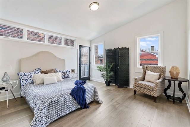 bedroom featuring light wood-style floors, lofted ceiling, multiple windows, and baseboards