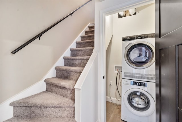 laundry area with baseboards, laundry area, wood finished floors, and stacked washer / drying machine