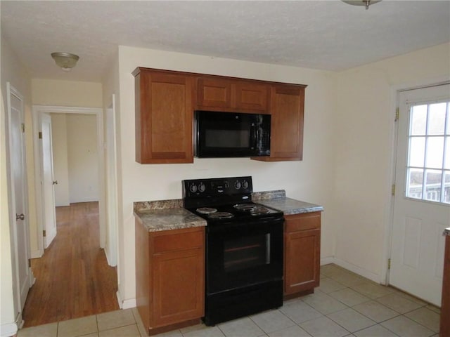 kitchen featuring baseboards, brown cabinetry, dark countertops, black appliances, and light tile patterned flooring