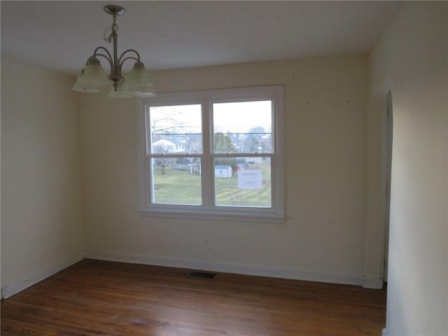 empty room featuring visible vents, baseboards, a chandelier, and dark wood-type flooring