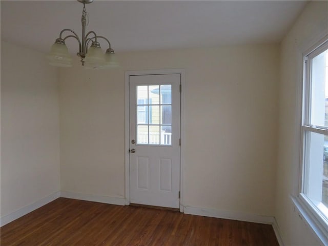 doorway featuring a notable chandelier, plenty of natural light, wood finished floors, and baseboards