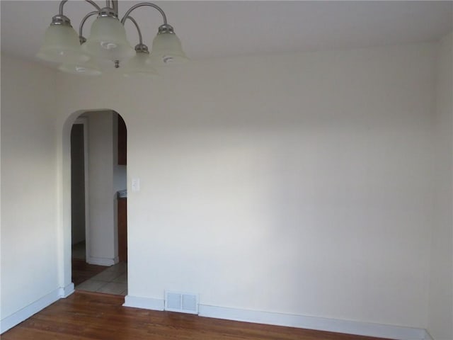 empty room featuring arched walkways, a notable chandelier, visible vents, wood finished floors, and baseboards