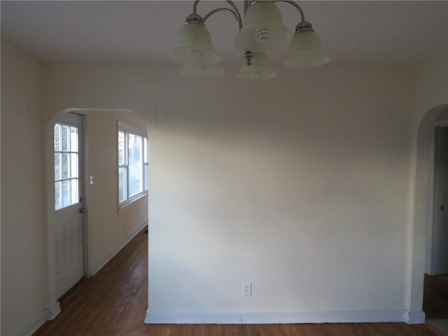 spare room featuring arched walkways, wood finished floors, and baseboards