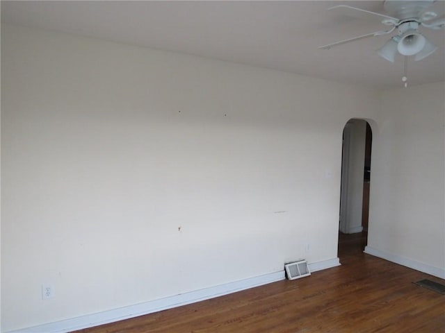 unfurnished room with arched walkways, wood finished floors, visible vents, and baseboards