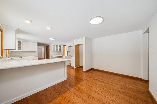 2972 Benshoff Hill Rd, Pa, PA 15909 - kitchen with white cabinetry, a sink, a peninsula, glass insert cabinets, and wood finished floors
