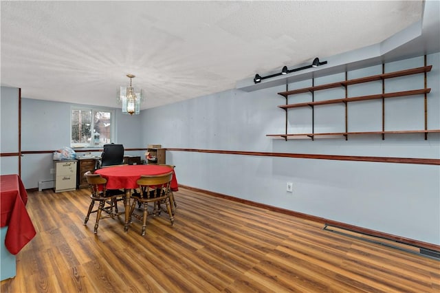 dining space with baseboards, dark wood-style flooring, a textured ceiling, a baseboard heating unit, and a notable chandelier