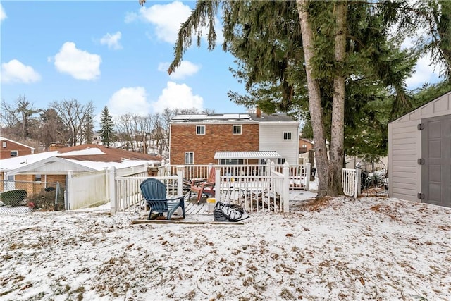 snow covered house featuring an outbuilding, brick siding, a storage unit, fence, and a deck