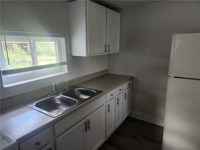 kitchen with white cabinets, dark wood-type flooring, freestanding refrigerator, a sink, and backsplash