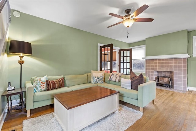 living area featuring a ceiling fan, light wood-type flooring, baseboards, and a tiled fireplace