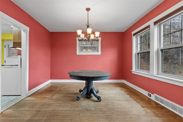 unfurnished dining area with visible vents, a notable chandelier, baseboards, and wood finished floors