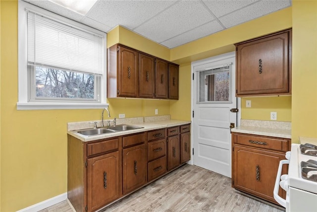 kitchen with a paneled ceiling, white range with gas stovetop, a sink, light countertops, and light wood-type flooring