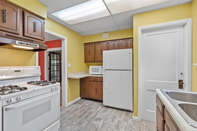 kitchen with white appliances, a drop ceiling, range hood, light countertops, and light wood-type flooring