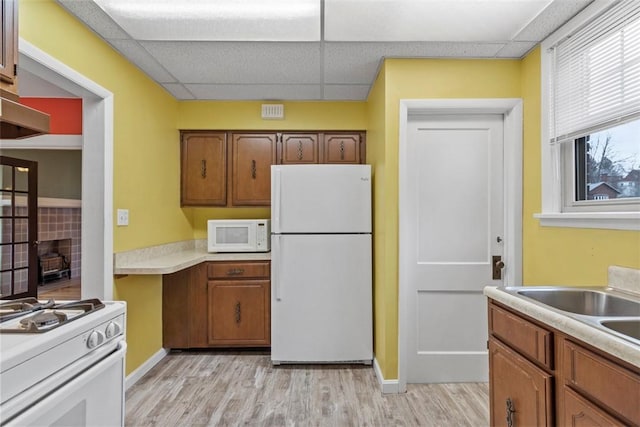 kitchen featuring white appliances, light wood finished floors, a drop ceiling, brown cabinets, and light countertops