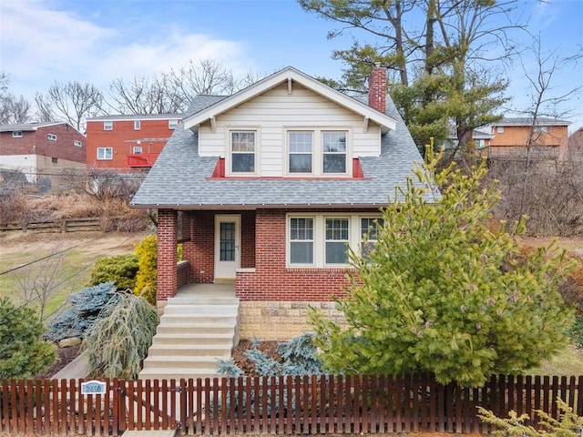 view of front of property with brick siding, roof with shingles, a chimney, and a fenced front yard