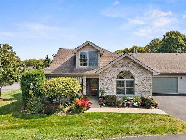 view of front facade featuring brick siding, a front yard, a shingled roof, and aphalt driveway