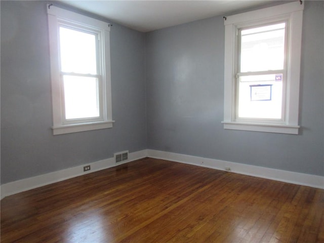 spare room with dark wood-style floors, visible vents, and baseboards