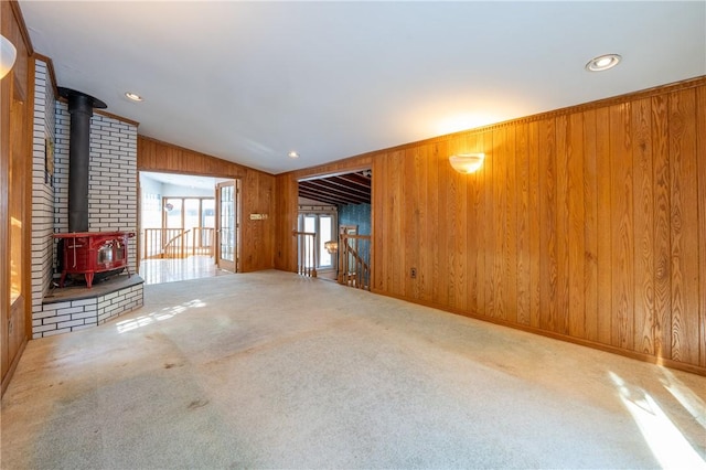 unfurnished living room featuring recessed lighting, carpet floors, wood walls, vaulted ceiling, and a wood stove