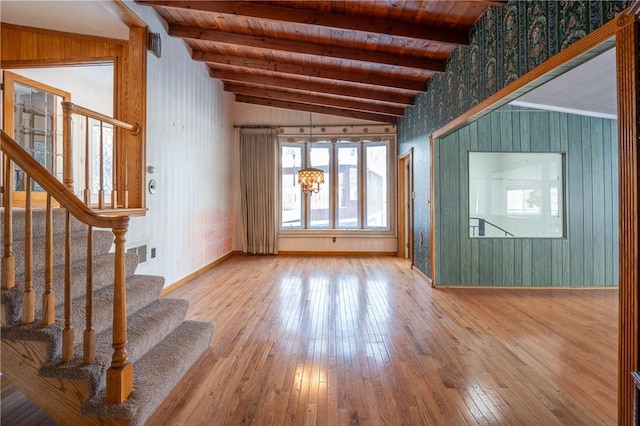 unfurnished living room with lofted ceiling with beams, hardwood / wood-style floors, wooden ceiling, baseboards, and stairs