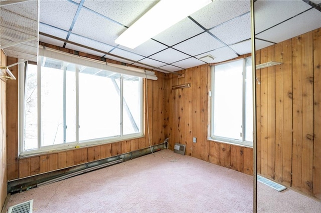 carpeted empty room with visible vents, wooden walls, and a drop ceiling