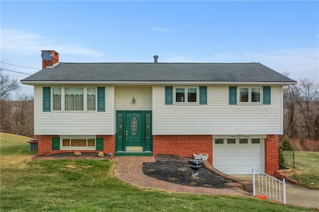 split foyer home featuring a garage, brick siding, a chimney, and a front yard