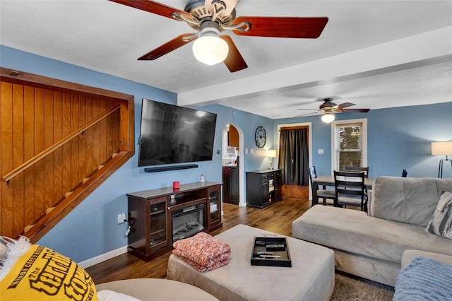 living area featuring arched walkways, dark wood finished floors, a ceiling fan, baseboards, and a glass covered fireplace