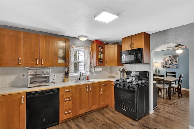 kitchen with brown cabinetry, glass insert cabinets, light countertops, black appliances, and a sink