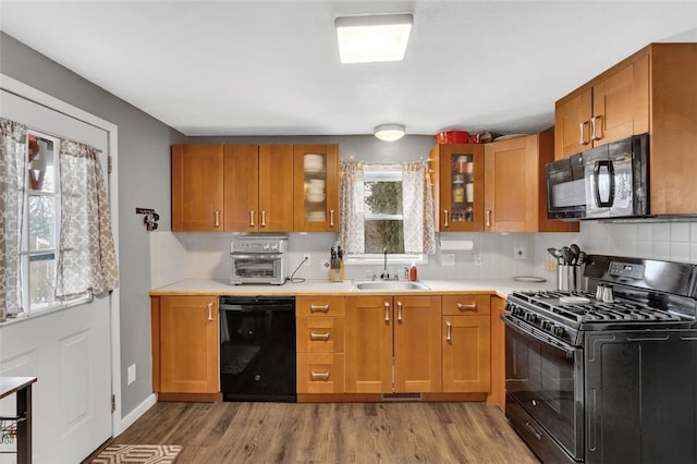 kitchen featuring glass insert cabinets, light countertops, a sink, and black appliances