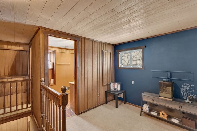 interior space with light colored carpet, wood walls, an upstairs landing, wooden ceiling, and baseboards