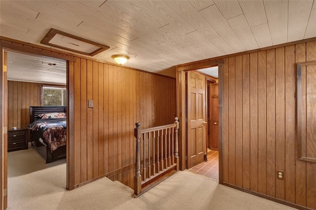 hallway with attic access, light carpet, wooden walls, and an upstairs landing