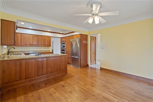 kitchen featuring brown cabinets, stainless steel appliances, light wood-style floors, a sink, and a peninsula