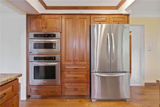 kitchen with light stone counters, brown cabinets, stainless steel appliances, ornamental molding, and light wood-type flooring