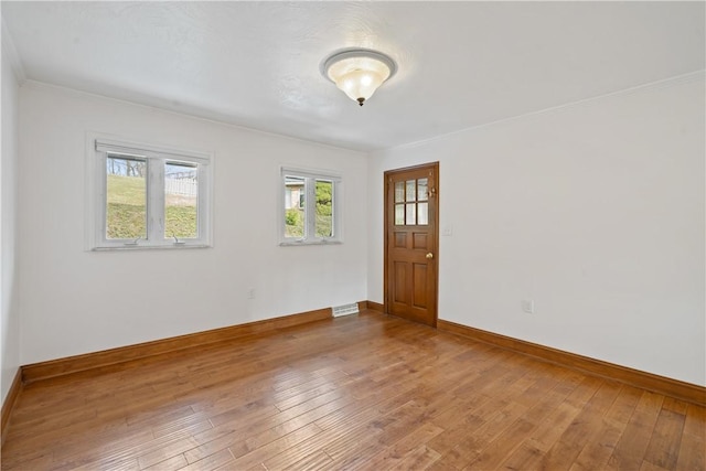 spare room featuring ornamental molding, wood-type flooring, visible vents, and baseboards