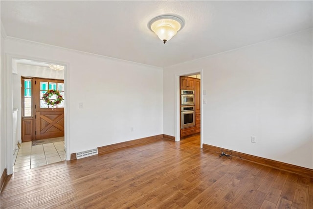 spare room with light wood-type flooring, visible vents, crown molding, and baseboards