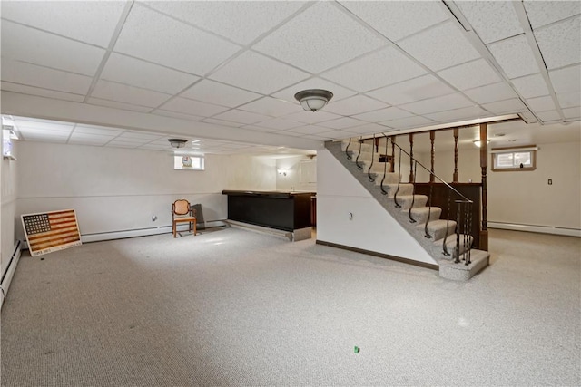 basement with a baseboard heating unit, stairway, a drop ceiling, and baseboards