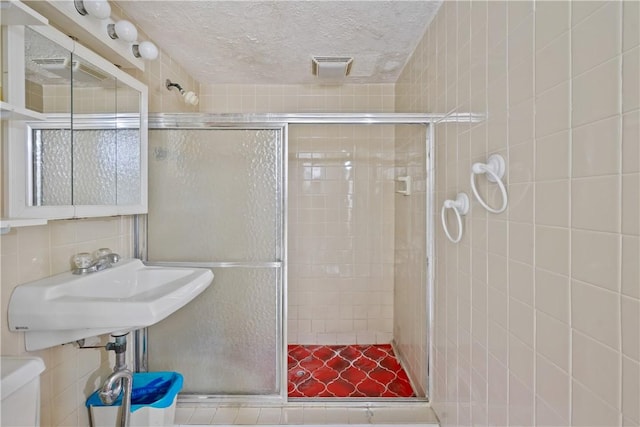 full bath with tile walls, visible vents, backsplash, a textured ceiling, and a shower stall