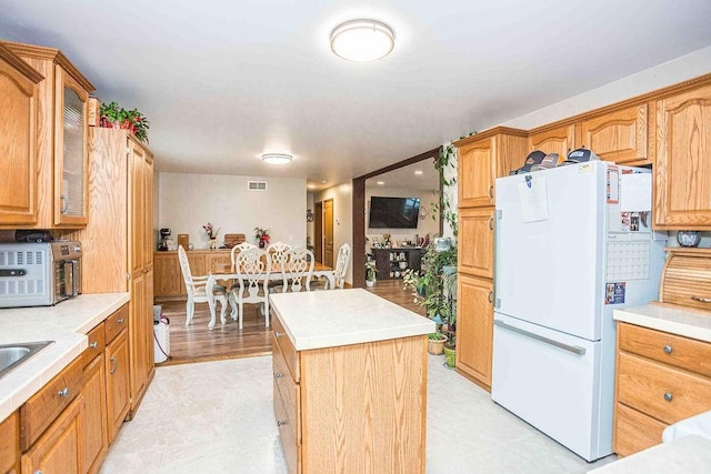 kitchen featuring a kitchen island, visible vents, light countertops, freestanding refrigerator, and glass insert cabinets