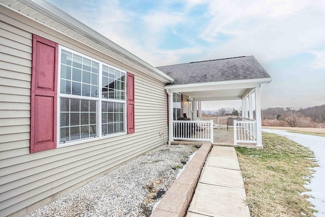 view of side of property with a porch and roof with shingles