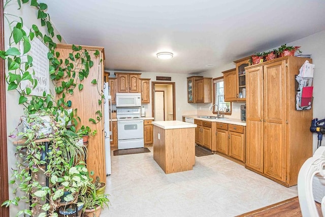 kitchen with white appliances, a kitchen island, glass insert cabinets, light countertops, and a sink