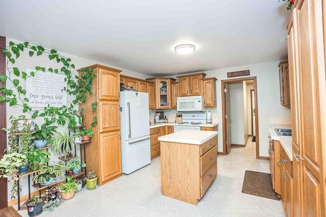 kitchen with white appliances, a kitchen island, light countertops, brown cabinetry, and glass insert cabinets