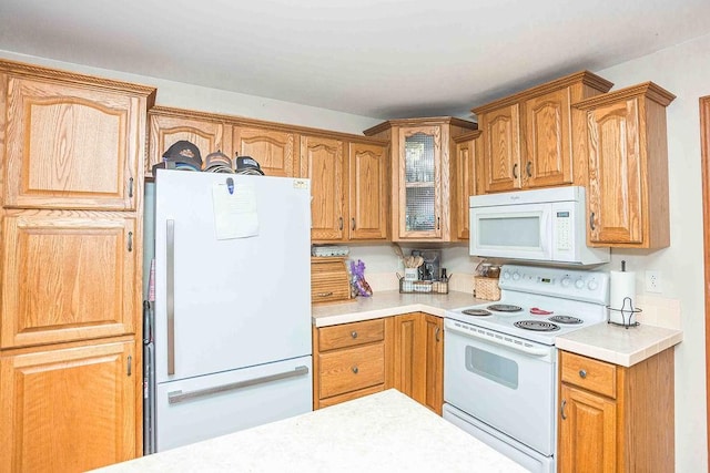 kitchen featuring glass insert cabinets, white appliances, light countertops, and brown cabinetry