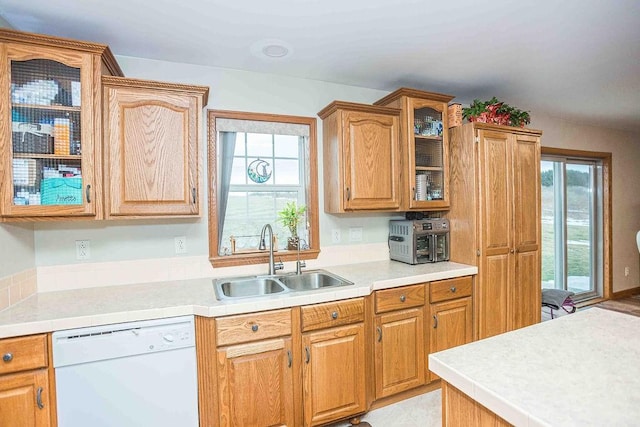 kitchen featuring a wealth of natural light, dishwasher, glass insert cabinets, light countertops, and a sink