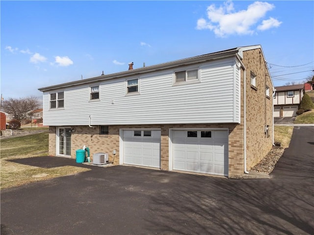 back of house featuring a garage, driveway, brick siding, and cooling unit