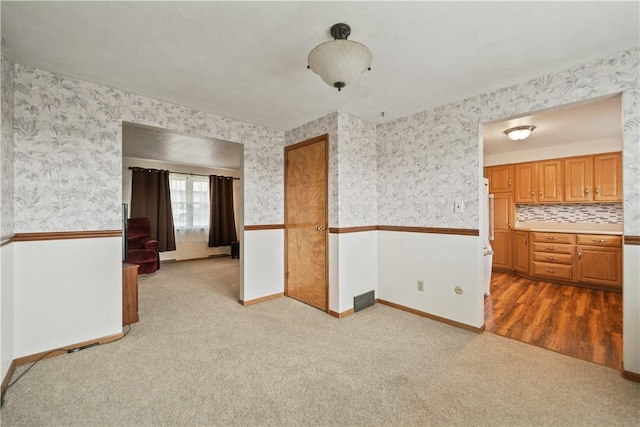 unfurnished room featuring light carpet, wainscoting, baseboards, and wallpapered walls