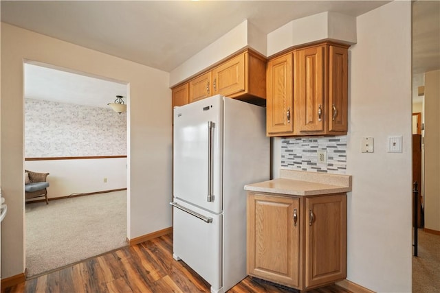 kitchen featuring tasteful backsplash, brown cabinets, dark wood-style flooring, freestanding refrigerator, and light countertops