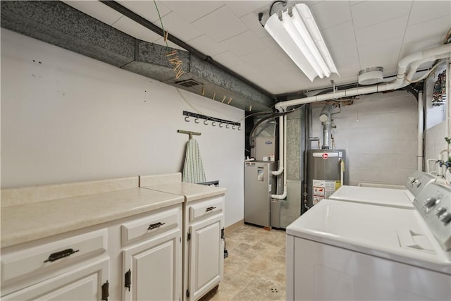 washroom featuring concrete block wall, gas water heater, heating unit, cabinet space, and washing machine and dryer