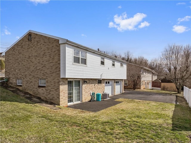 rear view of property with aphalt driveway, an attached garage, brick siding, fence, and a yard