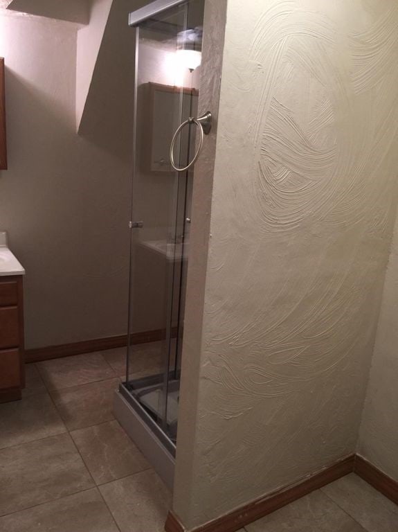 full bath featuring a stall shower, tile patterned flooring, vanity, and baseboards