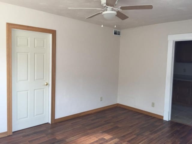 spare room featuring dark wood-type flooring, visible vents, baseboards, and a ceiling fan